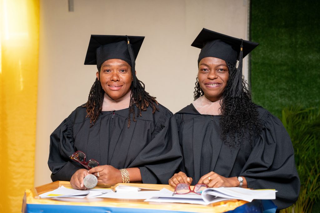 Two women in academic regalia seated at a ceremony table