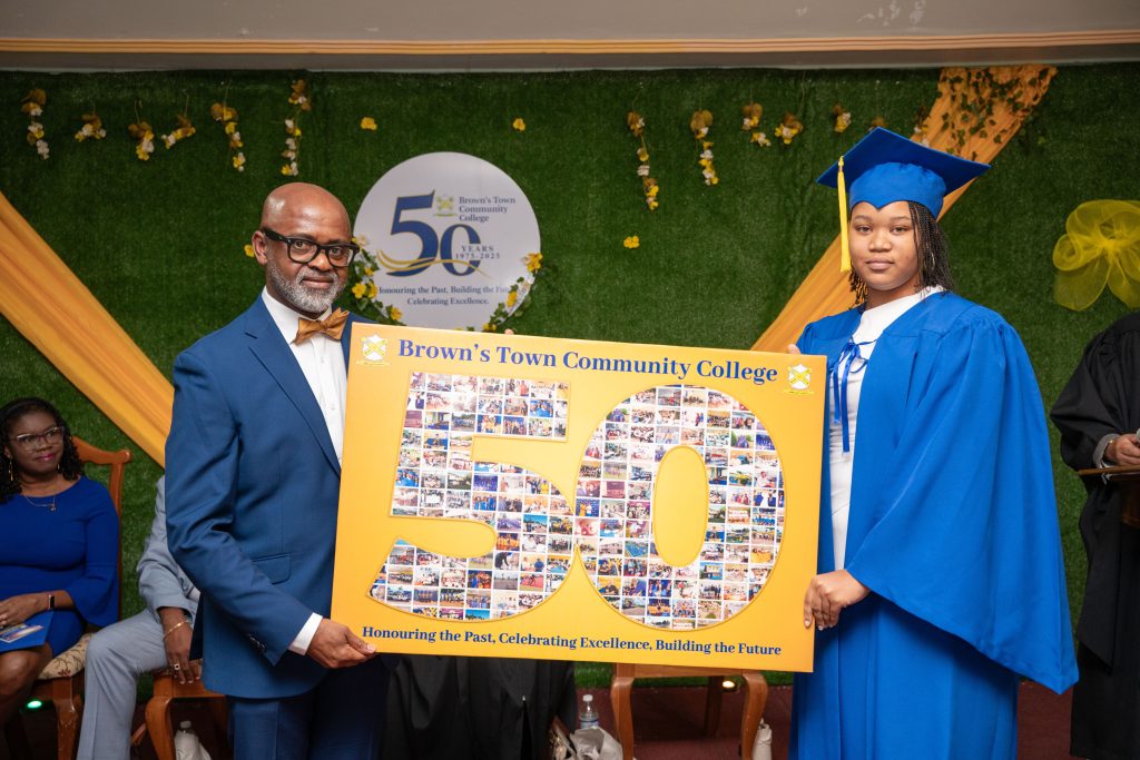 A graduate and presenter holding a commemorative college display